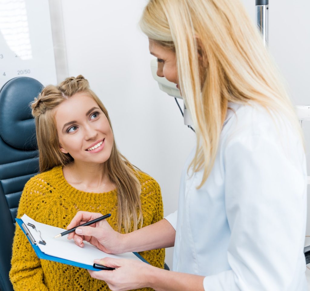 optometrist-writing-diagnosis-for-smiling-patient-in-clinic